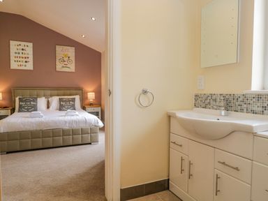 A bedroom with a bed and nightstands seen from a bathroom with a sink and mirror at Cartmel Lodge in Allithwaite near Grange-over-Sands