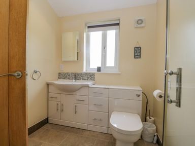 A bathroom with a sink vanity unit a toilet a window and a shower door at Cartmel Lodge in Allithwaite near Grange-over-Sands