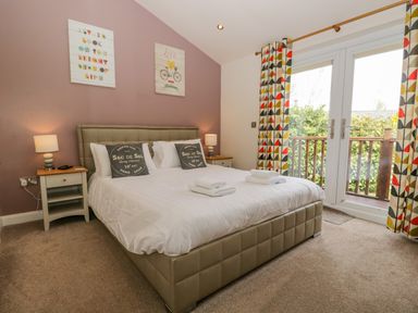 A bedroom with a double bed two bedside tables lamps patterned curtains and glass doors to a balcony at Cartmel Lodge in Allithwaite near Grange-over-Sands