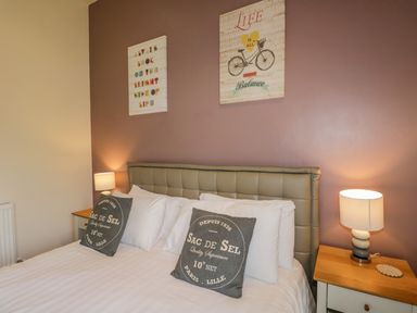 A bedroom with a double bed two pillows two bedside tables with lamps and wall art at Cartmel Lodge in Allithwaite near Grange-over-Sands