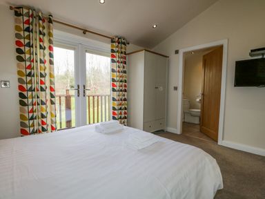 A bedroom with a bed, wardrobe, wall-mounted TV, and a bathroom entrance at Cartmel Lodge in Allithwaite near Grange-over-Sands