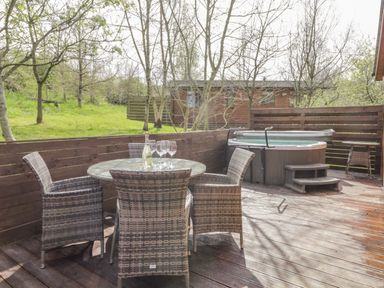 An outdoor wooden deck with a round glass table surrounded by four wicker chairs and a hot tub with steps