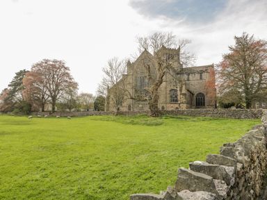 A historic stone building surrounded by trees and a grassy field with sheep near a stone wall at Cartmel Lodge in Allithwaite near Grange-over-Sands