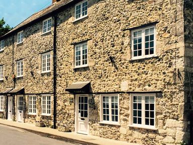 A stone exterior of a multi-story building with white framed windows and white doors at Craft Cottage in Beer near Seaton