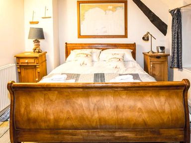 A wooden bed with a white quilt and pillows between two wooden nightstands with lamps in a bedroom at Craft Cottage in Beer near Seaton
