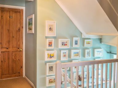A staircase with white railings and a gallery wall of framed pictures next to a wooden door at Craft Cottage Beer near Seaton