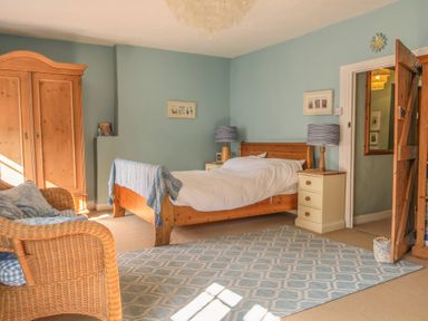 A bedroom with a wooden bed white bedding two bedside tables with lamps a wicker chair and a wooden wardrobe at Craft Cottage in Beer near Seaton