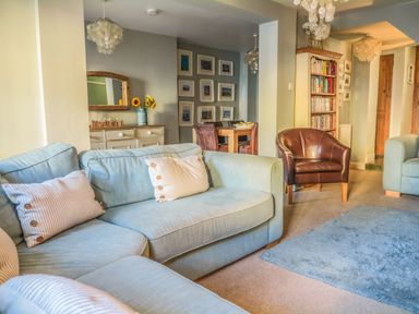 A living room with blue sofas a brown armchair a dining table with chairs a sideboard with sunflowers and pictures on the wall at Craft Cottage Beer near Seaton