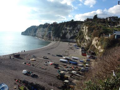 A rocky beach with boats and trailers near cliffs and houses at Craft Cottage in Beer near Seaton