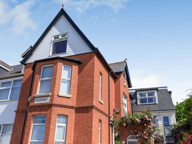 A red brick house with multiple windows and a stairway with flowers in front at Glenwood in Woolacombe