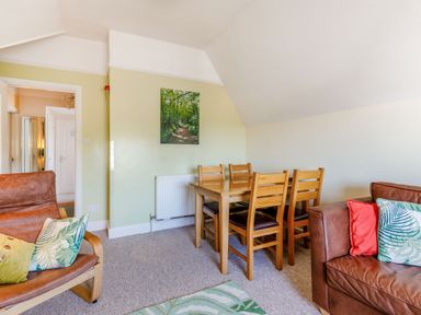 A living and dining area with wooden dining table and chairs leather seating with cushions and a wall painting at Glenwood in Woolacombe