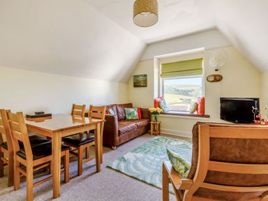 A sitting room with a wooden dining table and chairs and a brown sofa near a window at Glenwood in Woolacombe
