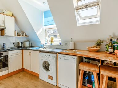 A kitchen with white cabinets a washing machine dishwasher and a countertop bar with stools at Glenwood in Woolacombe