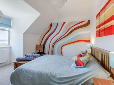 A bedroom with a bed pillow lamps chair and window with blue blind at Glenwood in Woolacombe