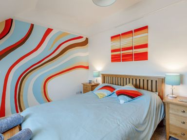 A bedroom with a double bed wooden headboard two bedside tables with lamps and a colorful wall mural at Glenwood in Woolacombe