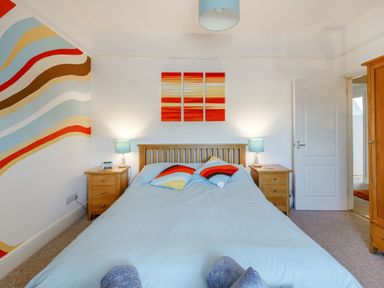 A bedroom with a bed between two wooden nightstands and colorful wavy wall art at Glenwood in Woolacombe