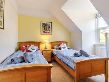 A bedroom with two single beds with blue striped bedding a bedside table with a lamp and a window at Glenwood in Woolacombe