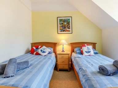 A bedroom with two single beds with blue striped bedding a wooden nightstand and a lamp at Glenwood in Woolacombe