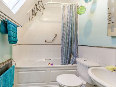 A bathroom with a bathtub shower with striped curtain a toilet a sink and blue towels at Glenwood in Woolacombe