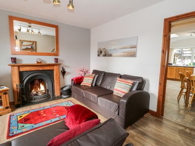 A living room with a fireplace a brown leather sofa a colorful rug and a kitchen visible through a doorway at Ty Gwynn in Tanygrisiau