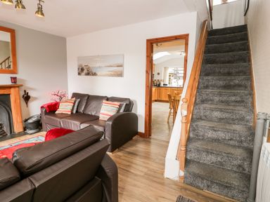 A living room with brown leather sofas a carpeted staircase and a view into a kitchen at Ty Gwynn in Tanygrisiau