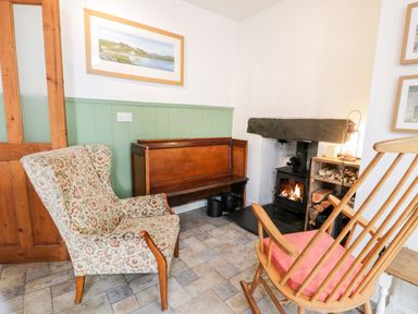 A room with a floral armchair a wooden bench a rocking chair in front of a fireplace with stacked firewood at Ty Gwynn in Tanygrisiau