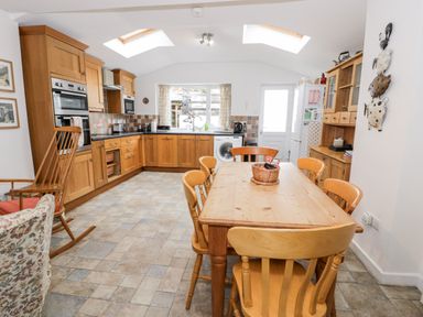 A kitchen with wooden cabinets a dining table with chairs and a rocking chair at Ty Gwynn in Tanygrisiau