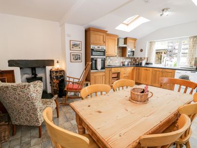 A kitchen and dining area with wooden cabinets a dining table with chairs a floral armchair and a rocking chair at Ty Gwynn in Tanygrisiau