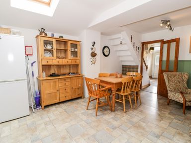 A dining area with a wooden table and six chairs a wooden cabinet a white refrigerator and an armchair at Ty Gwynn in Tanygrisiau