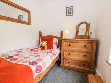 A bedroom with a wooden bed with patterned bedding a chest of drawers with a mirror and lamp at Ty Gwynn in Tanygrisiau