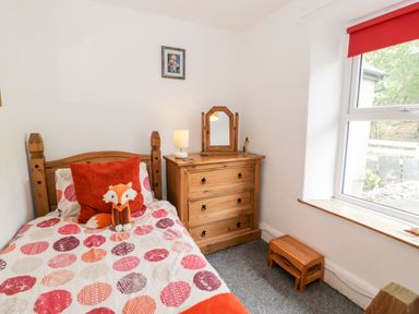 A bedroom with a single bed a stuffed fox toy a wooden dresser with a mirror and a window with a red blind at Ty Gwynn in Tanygrisiau