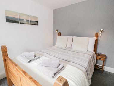 A bedroom with a wooden bed two pillows two folded towels on the bed a small bedside table with a clock and wall art above the bed at Ty Gwynn in Tanygrisiau