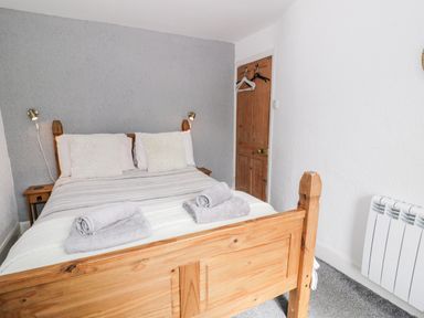 A bedroom with a wooden bed frame with pillows and folded towels near a wooden door at Ty Gwynn in Tanygrisiau