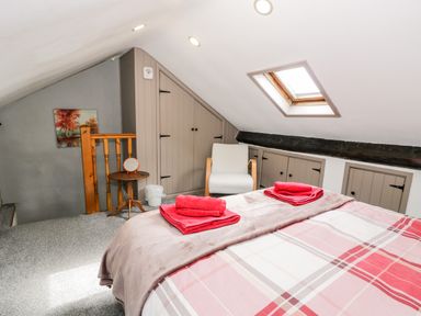 A bedroom with a bed covered in a plaid blanket and red towels on top a white armchair a small round wooden table with a mirror a skylight window and built in cupboards at Ty Gwynn in Tanygrisiau