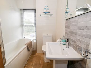 A bathroom with a bathtub a toilet a sink a towel on the bathtub and a sailboat decoration on a glass shelf at Ty Gwynn in Tanygrisiau