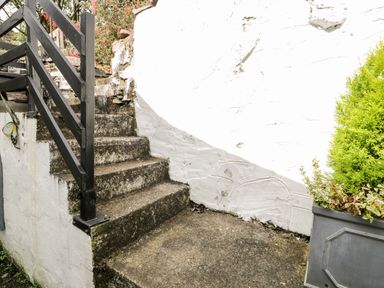An outdoor concrete stairway with black railing next to a white wall and a gray planter with green plants at Ty Gwynn in Tanygrisiau