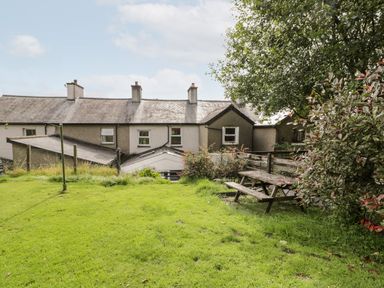 A backyard with grass a wooden picnic table and bushes behind a row of houses at Ty Gwynn in Tanygrisiau