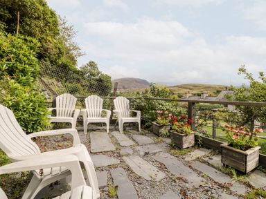 An outdoor patio with white plastic chairs and wooden flower boxes overlooking a rural landscape at Ty Gwynn in Tanygrisiau