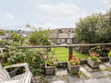 A balcony with potted plants and plastic chairs overlooking a grassy garden and houses at Ty Gwynn in Tanygrisiau
