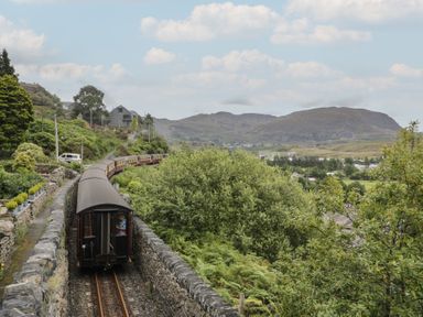 A train traveling along tracks near mountains and greenery at Ty Gwynn in Tanygrisiau