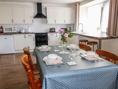 A kitchen with a dining table set with plates and bowls and a vase with flowers at Marsh Cottage in North Molton