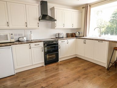 A kitchen with white cabinets black oven microwave and window at Marsh Cottage in North Molton