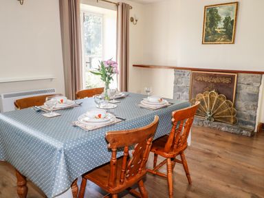 A dining room with a table set for four on a blue polka dot tablecloth wooden chairs a stone fireplace and a painting above at Marsh Cottage in North Molton
