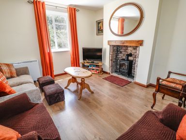 A living room with a wooden coffee table a TV on a stand a fireplace with a mirror above orange curtains and sofas at Marsh Cottage in North Molton