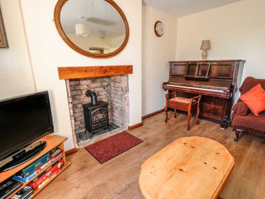A living room with a fireplace stove television piano coffee table and a sofa at Marsh Cottage in North Molton