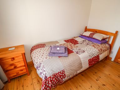 A single bed with patchwork bedding and folded towels next to a wooden bedside table in a bedroom at Marsh Cottage in North Molton