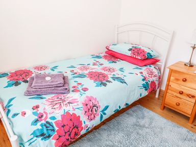 A single bed with floral bedding and folded towels next to a wooden nightstand with a lamp at Marsh Cottage in North Molton