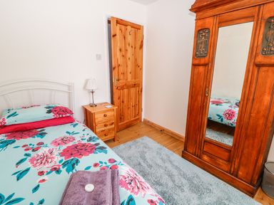 A bedroom with a bed floral bedspread a wooden wardrobe with mirror a bedside table and a lamp at Marsh Cottage in North Molton