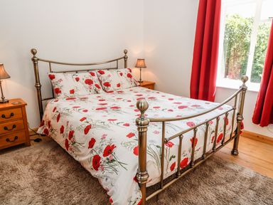 A bedroom with a metal bed frame floral bedding two wooden nightstands with lamps and red curtains at Marsh Cottage in North Molton