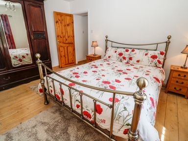 A bedroom with a metal bed frame and floral bedding two wooden nightstands with lamps a wooden wardrobe with a mirror and a wooden door at Marsh Cottage in North Molton